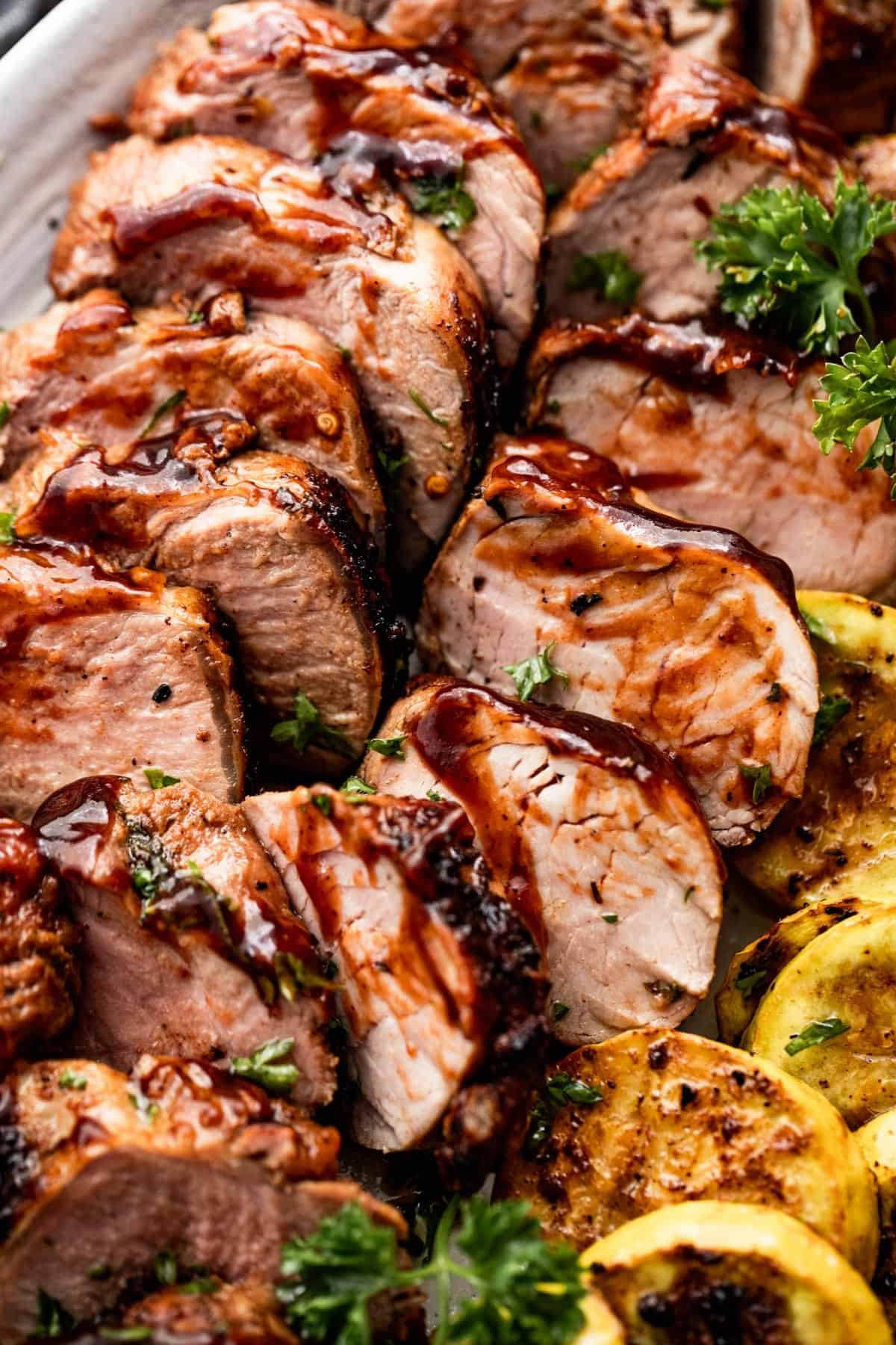 grilled pork tenderloin, sliced, and arranged on an oval platter alongside sliced and grilled yellow squash.