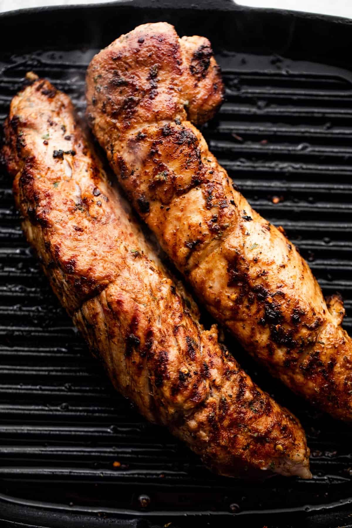 grilling two pork tenderloins, side by side, on a black grill pan.