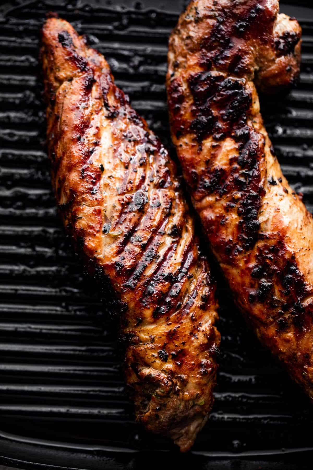 grilling two pork tenderloins, side by side, on a black grill pan.