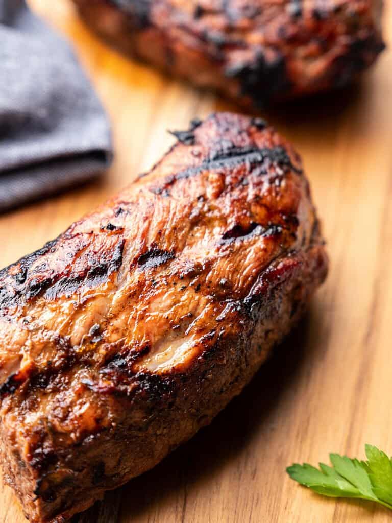 Freshly grilled pork on a cutting board beside a cloth napkin