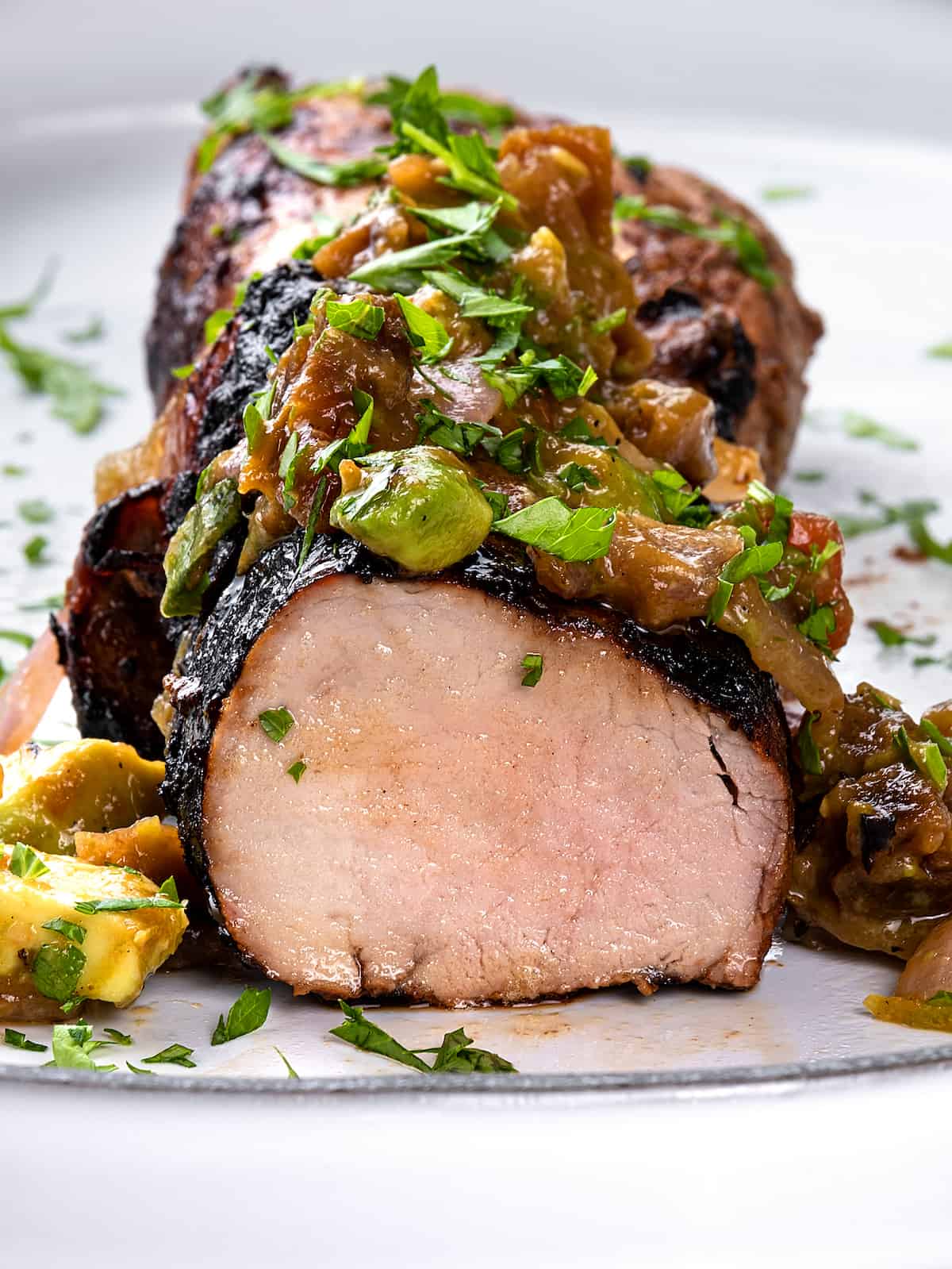 Slices of grilled pork tenderloin on a plate with avocado salsa on top of the pork