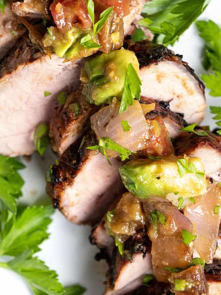 A close-up shot of sliced pork with avocado apricot salsa spooned over it