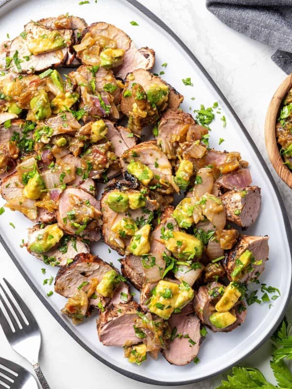 A serving plate holding a batch of grilled pork tenderloin covered in apricot salsa