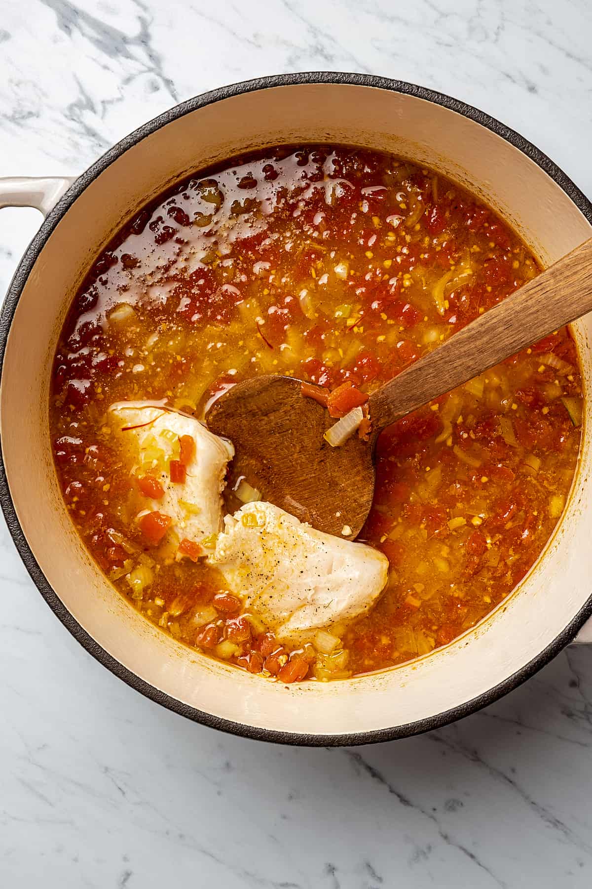 Fish pieces added to a pot of tomato-based soup.