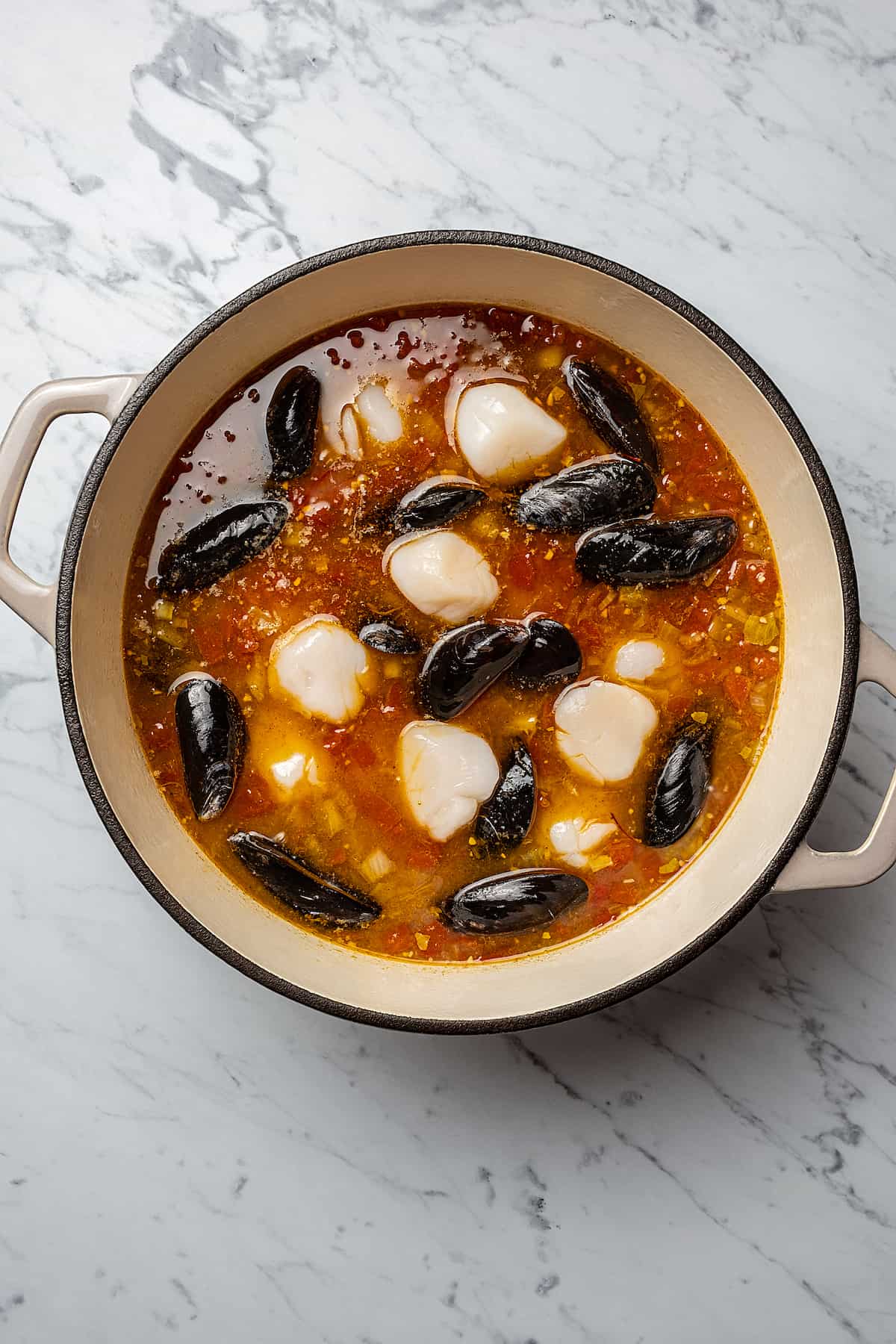 Fish and mussels arranged in a Dutch oven full of cooking soup.