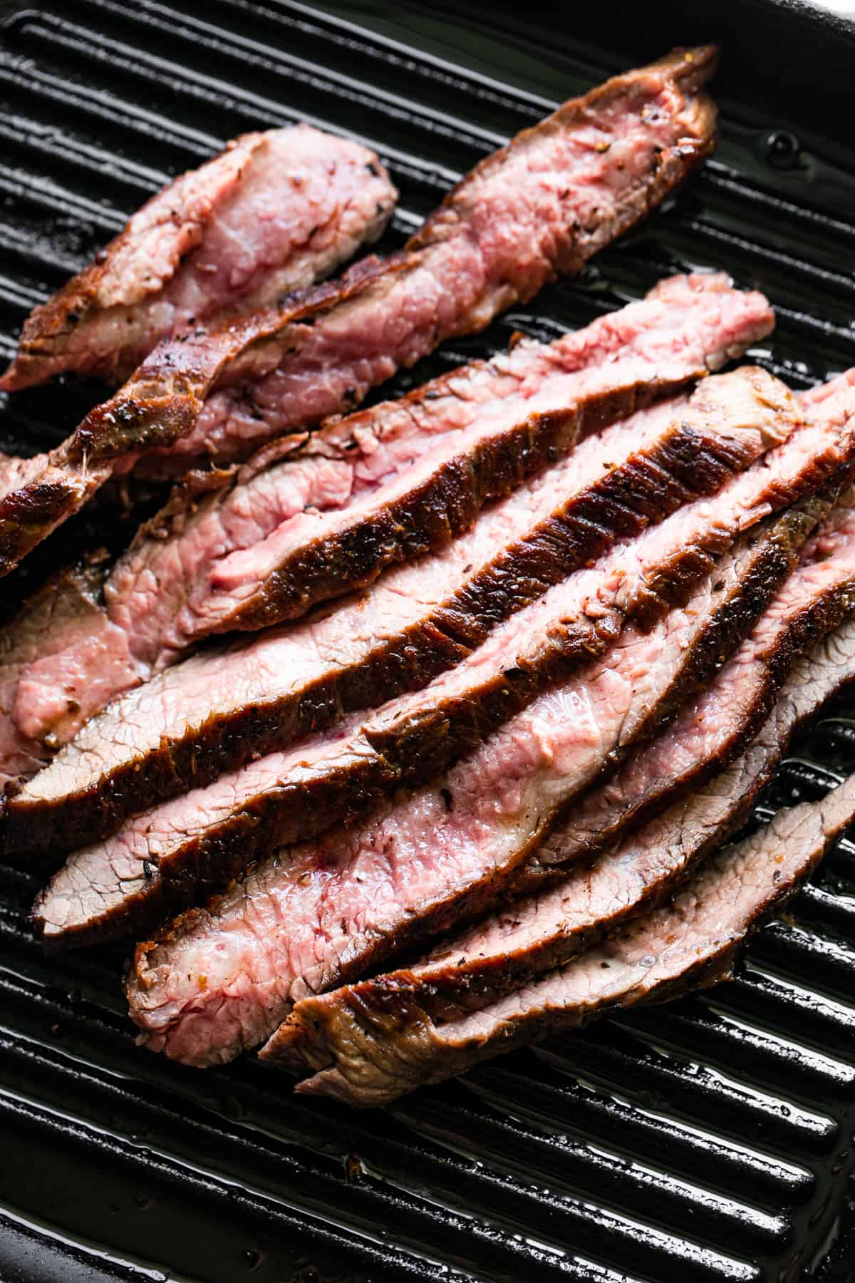 black grill pan with slices of flank steak arranged inside the pan.