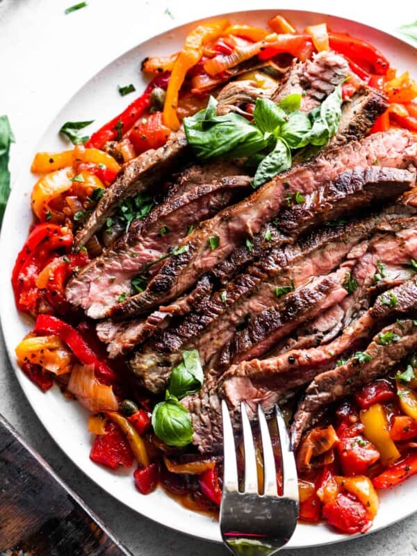slices of grilled flank steak served over a bed of peperonata, with a large serving fork placed at the bottom of the plate.