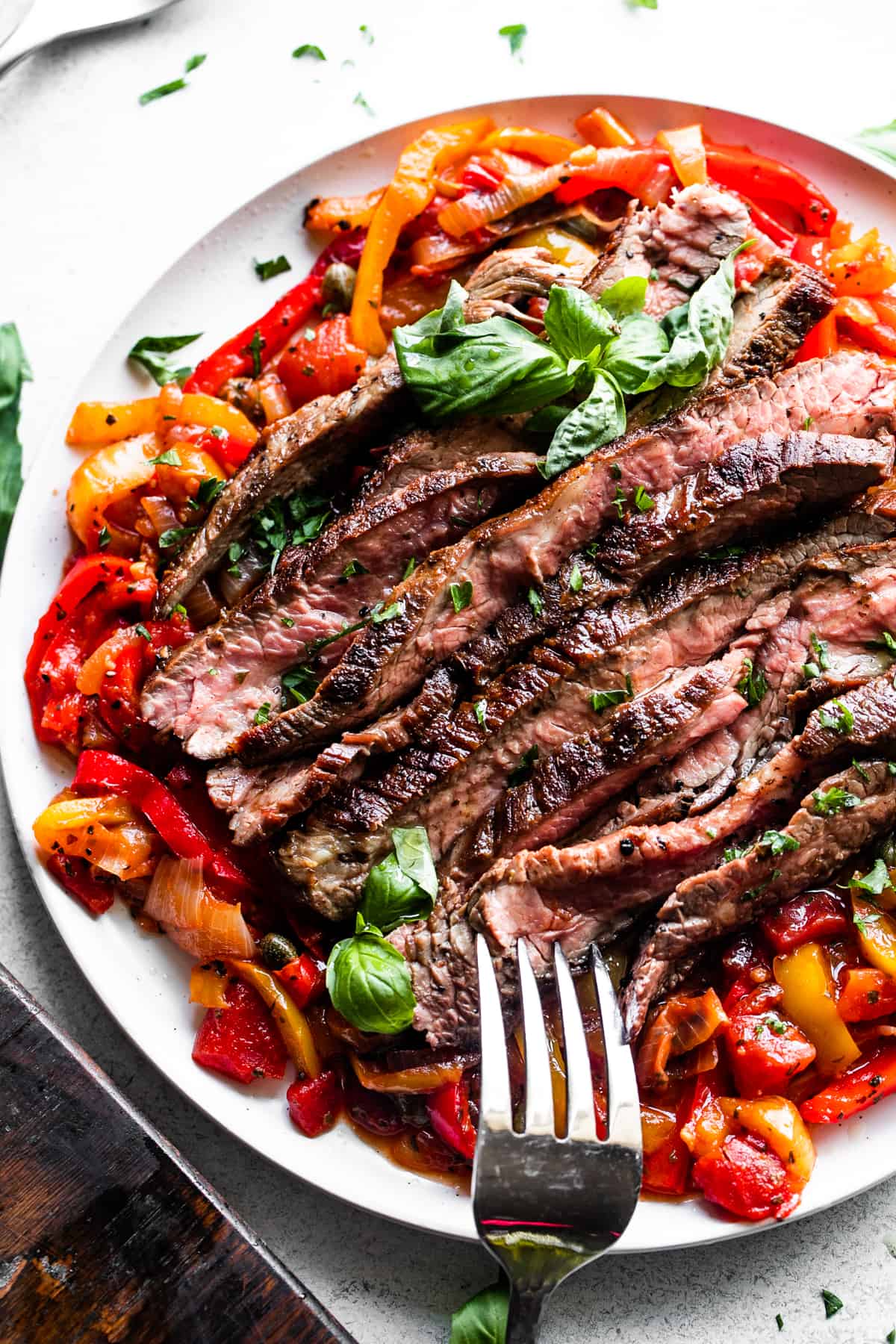 slices of grilled flank steak served over a bed of peperonata, with a large serving fork placed at the bottom of the plate.