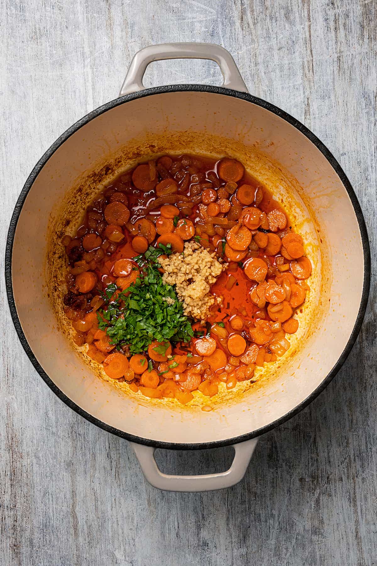 Carrots, parsley, garlic, and other soup ingredients in a Dutch oven.