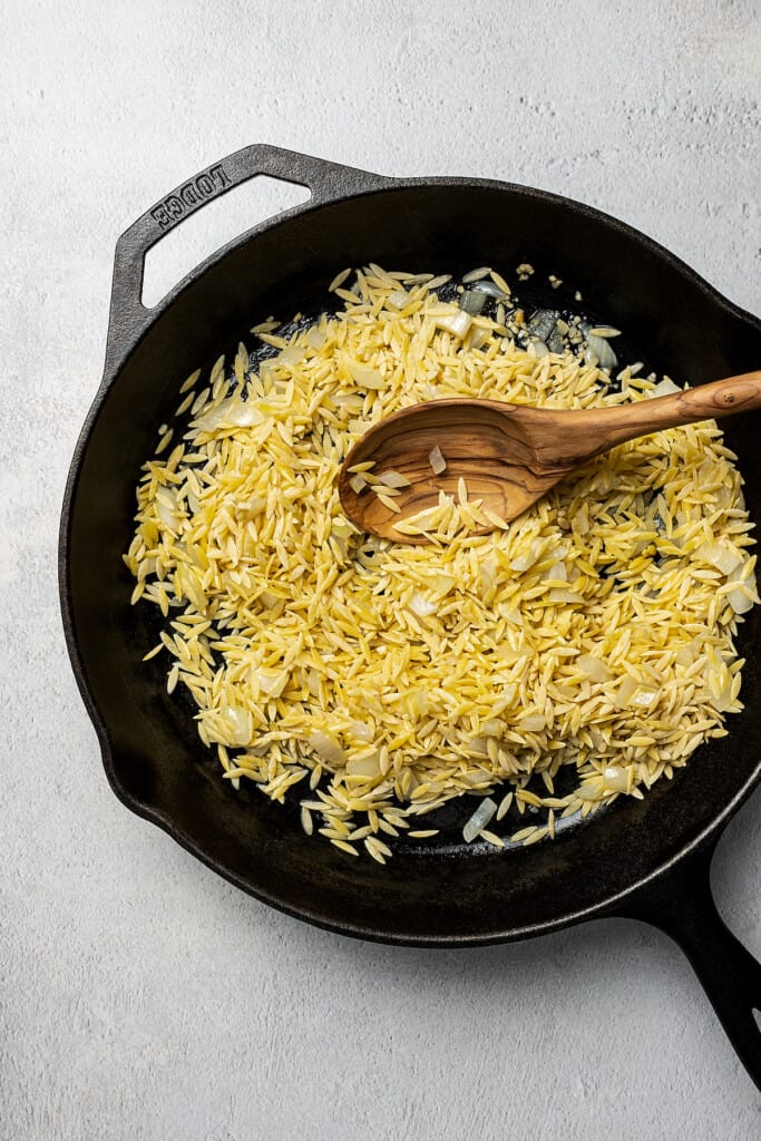 Dry orzo and aromatics cooking in a skillet.