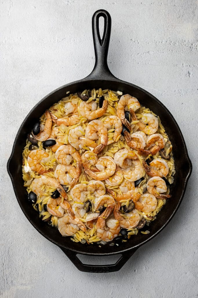 A skillet of pasta and shrimp with black olives and feta.