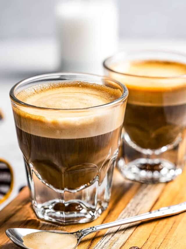 Side shot of two coffee glass mugs filled with cortado coffee.