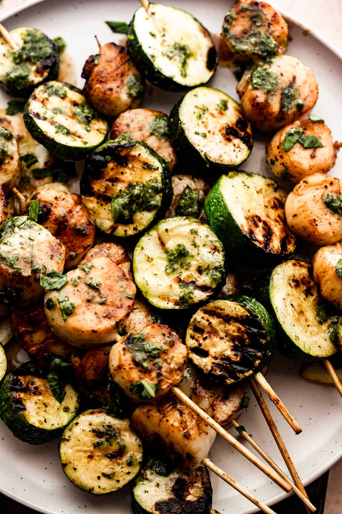 Closeup image of grilled zucchini skewers and grilled scallop skewers on a plate drizzled with garlic basil dressing.