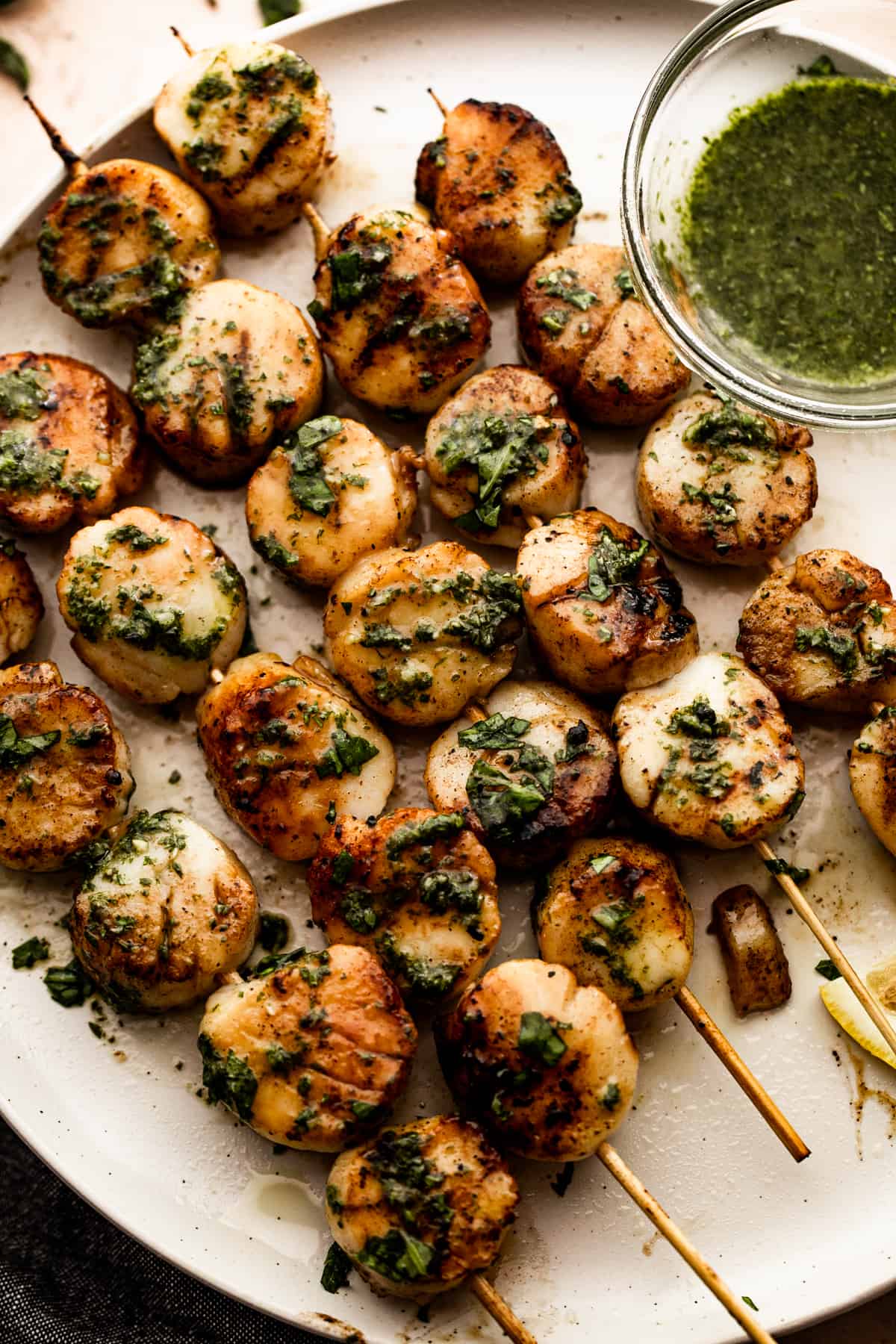 Grilled scallop skewers on a plate with basil garlic sauce.