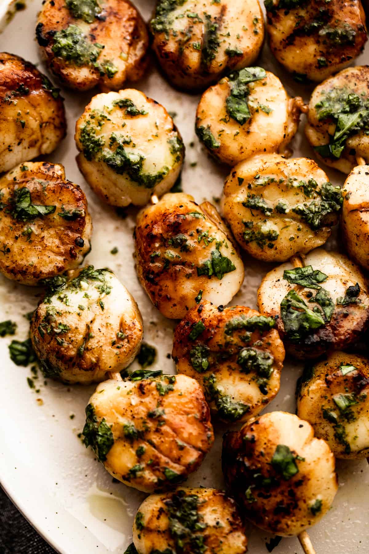Closeup image of grilled scallop skewers on a plate with basil garlic dressing.
