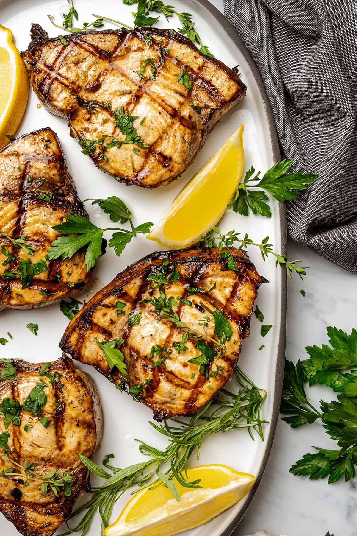  four grilled swordfish steaks on a serving platter with lemon wedges