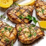 four grilled swordfish steaks on a serving platter with lemon wedges