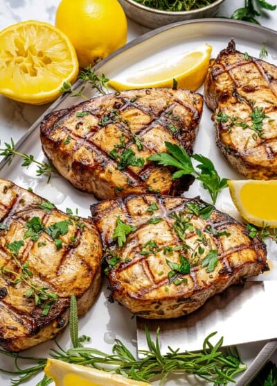 four grilled swordfish steaks on a serving platter with lemon wedges