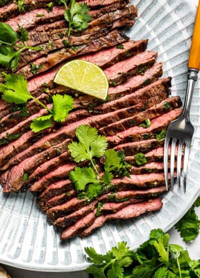 Sliced carne asada on a plate with a serving fork