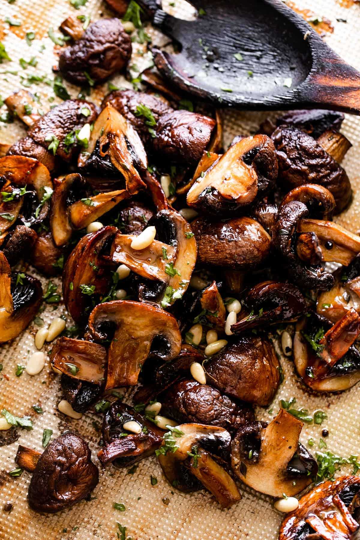 overhead shot of a wooden spoon stirring through roasted mushrooms.
