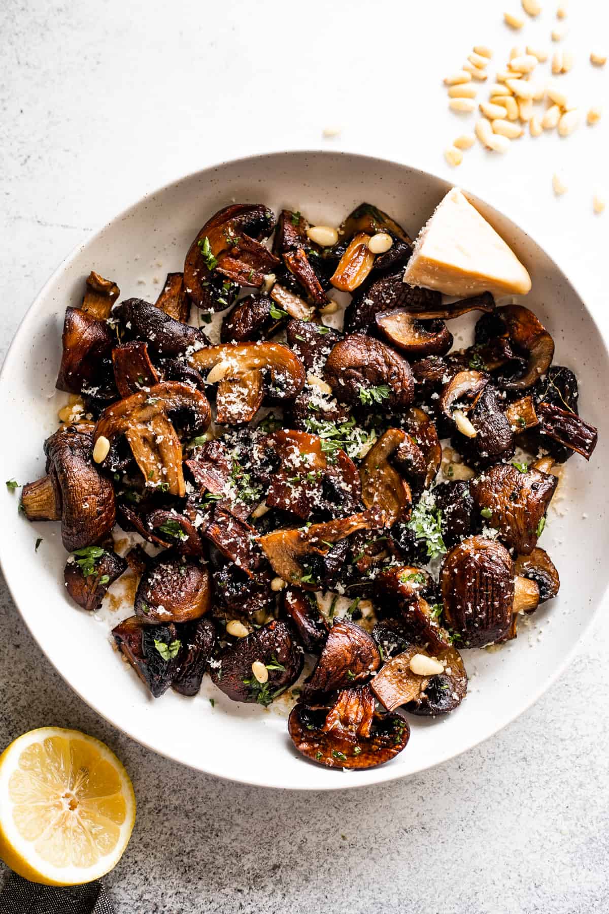 white serving bowl with Roasted Mushrooms topped with grated Parmesan cheese and Pine Nuts.