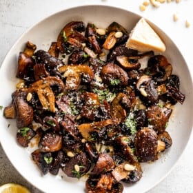 white serving bowl with Roasted Mushrooms topped with grated Parmesan cheese and Pine Nuts.