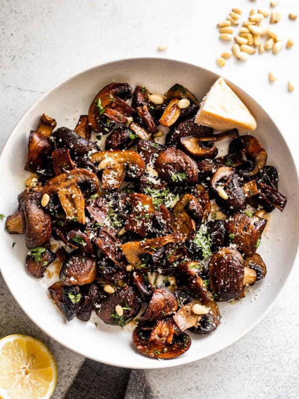 white serving bowl with Roasted Mushrooms topped with grated Parmesan cheese and Pine Nuts.