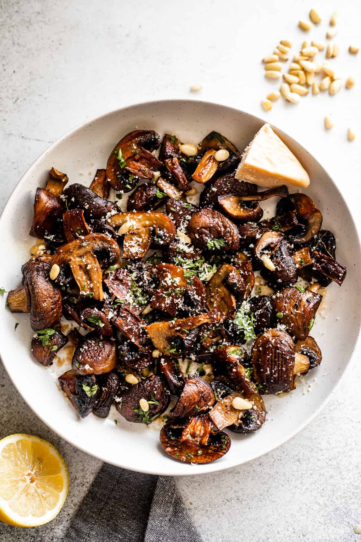 white serving bowl with Roasted Mushrooms topped with grated Parmesan cheese and Pine Nuts.