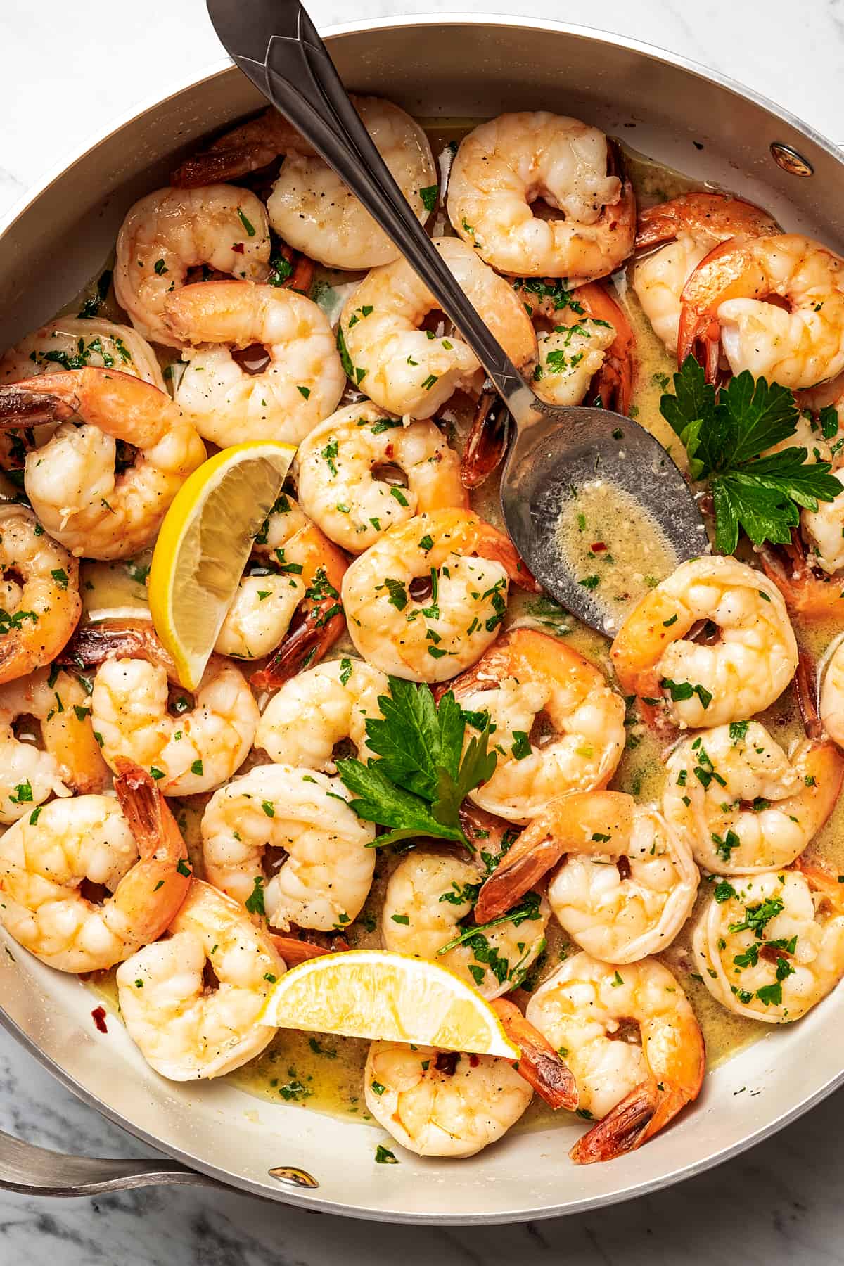 Shrimp scampi in a skillet, with a big spoon placed inside to spoon out shrimp.