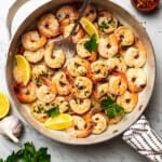 Shrimp scampi in a skillet, with a big spoon placed inside to spoon out shrimp.