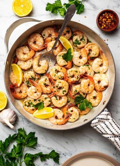 Shrimp scampi in a skillet, with a big spoon placed inside to spoon out shrimp.