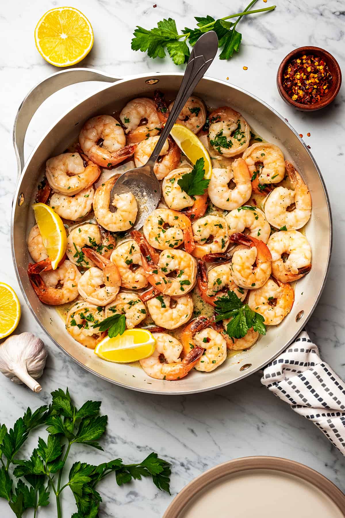 Shrimp scampi in a skillet, with a big spoon placed inside to spoon out shrimp.