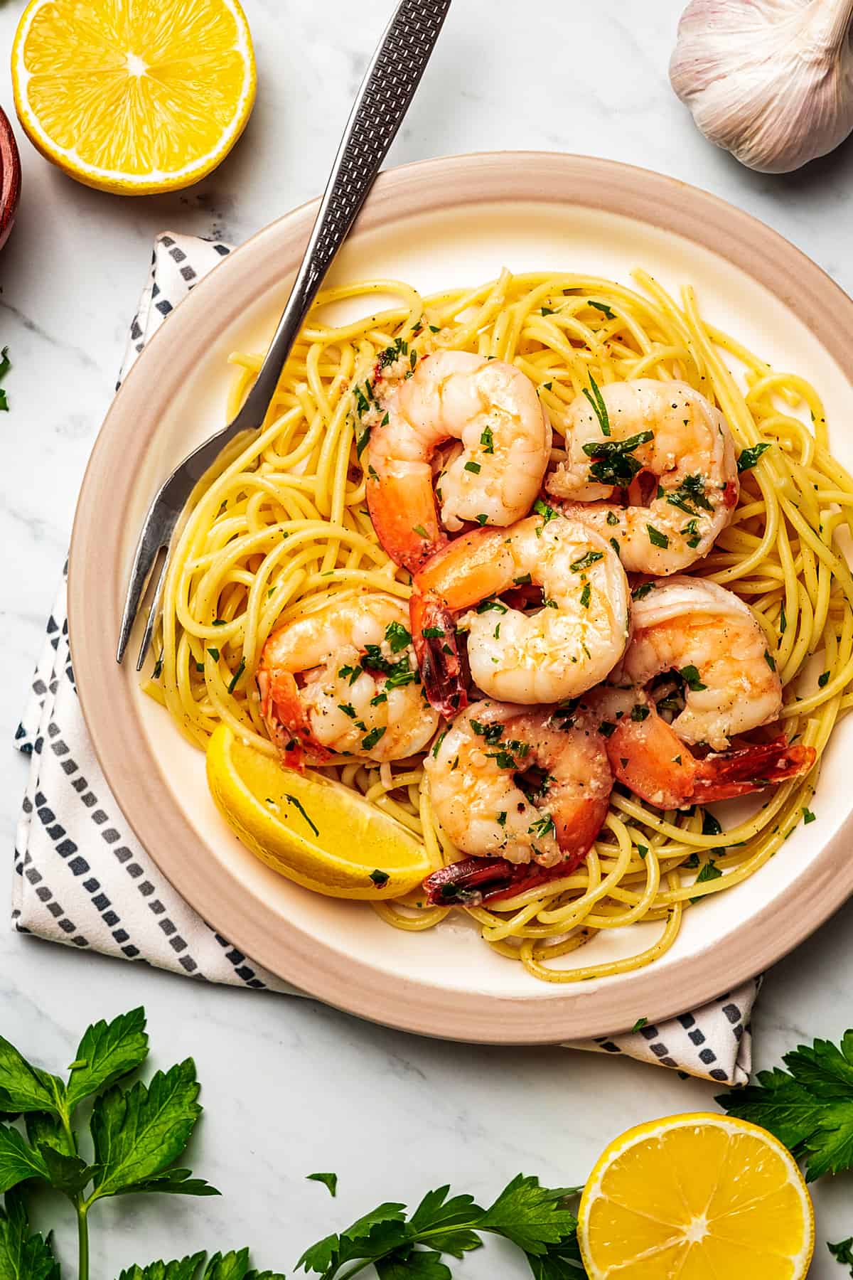 Shrimp scampi on top of spaghetti with lemon wedges