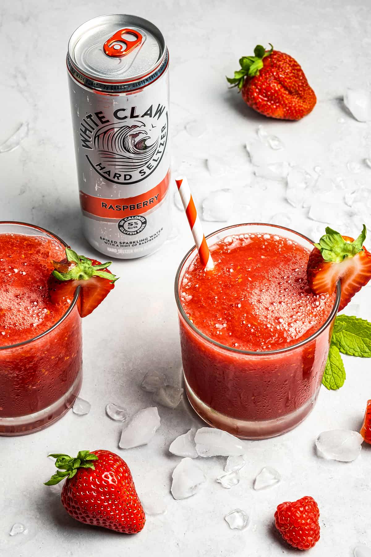 two white claw slushies in a glass next to berries and a can of White Claw.