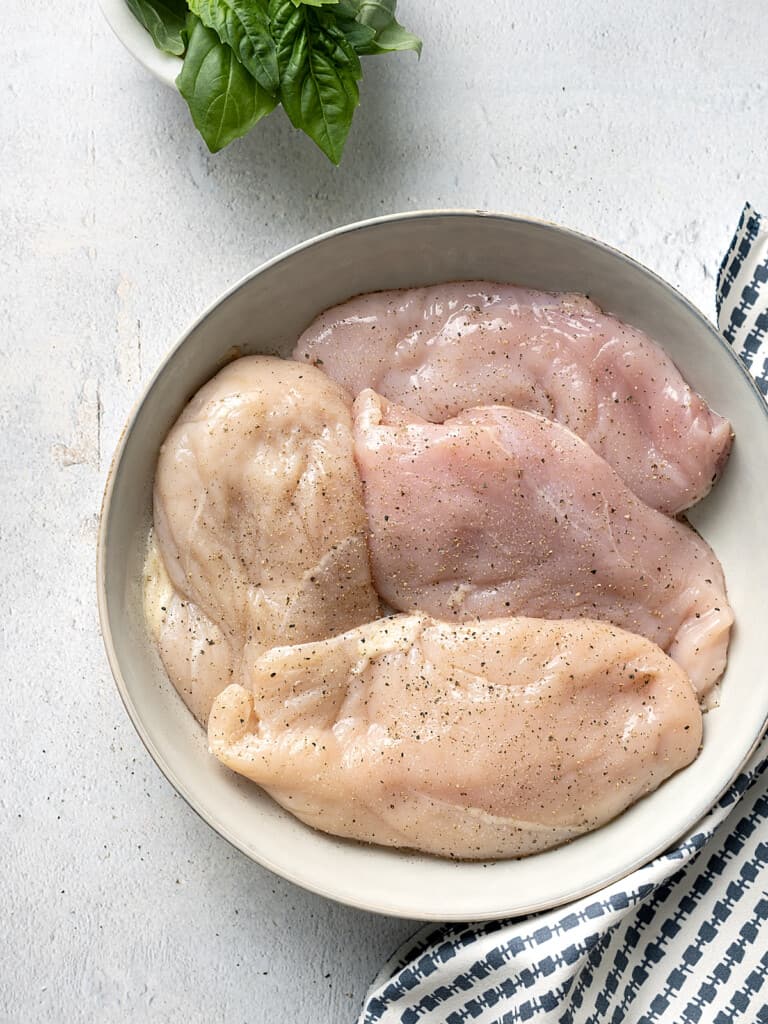 Boneless chicken breasts in a bowl seasoned with salt and pepper.