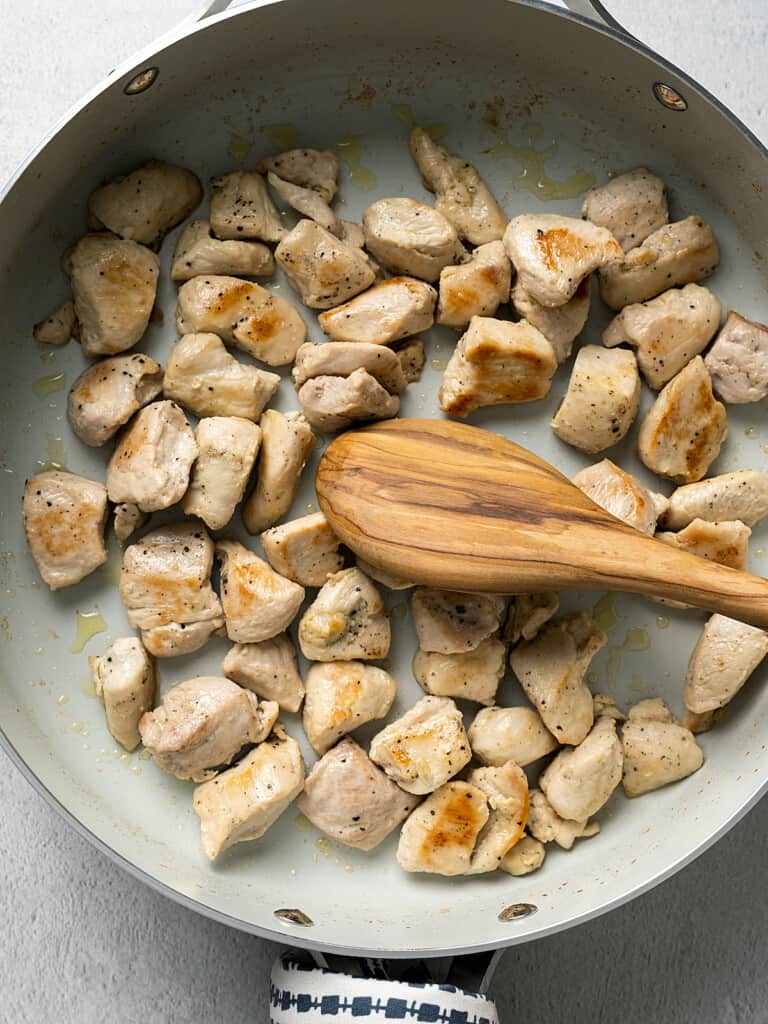 Chicken beginning to brown as it's sauteed in a pan on the stove.