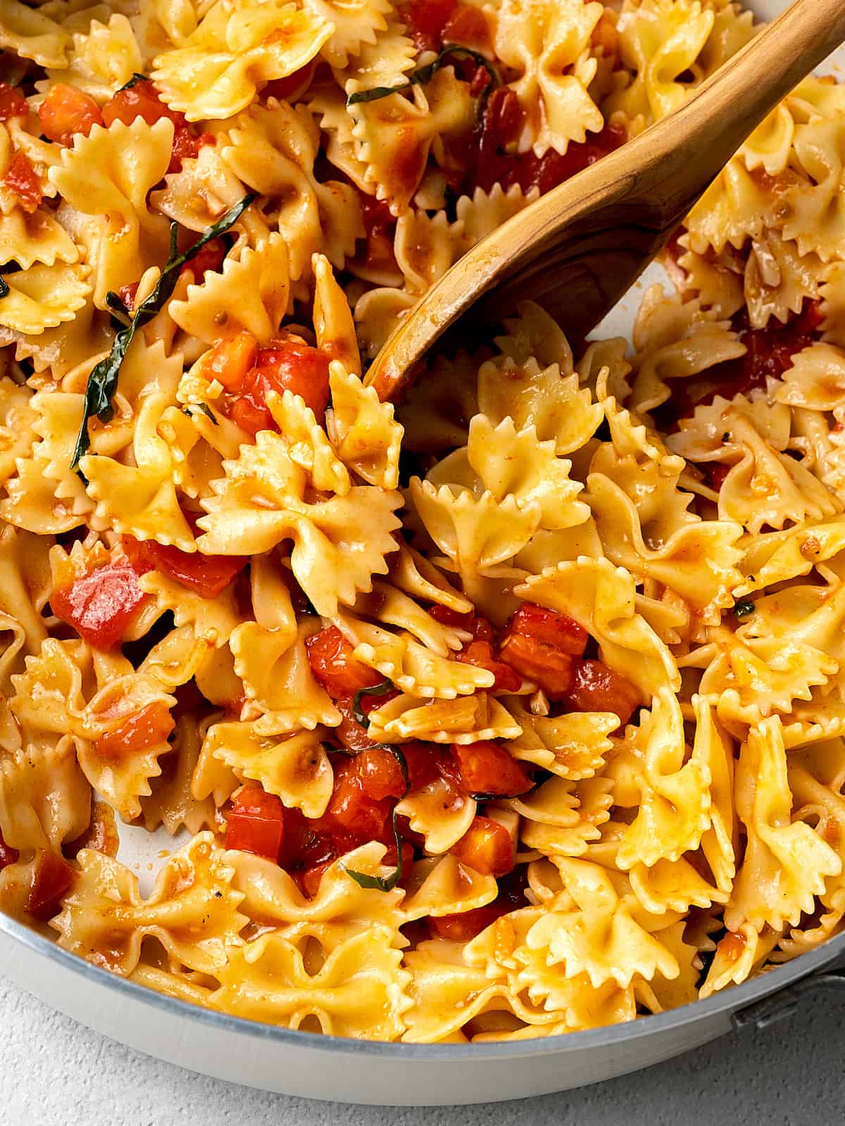 A wooden spoon stirring pasta into bruschetta sauce.