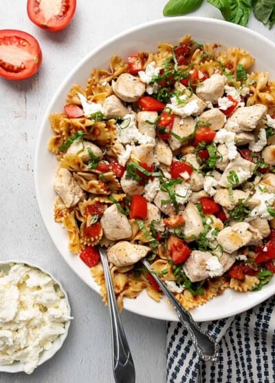 Sauteed chicken laid over bruschetta pasta next to a bowl of cheese.
