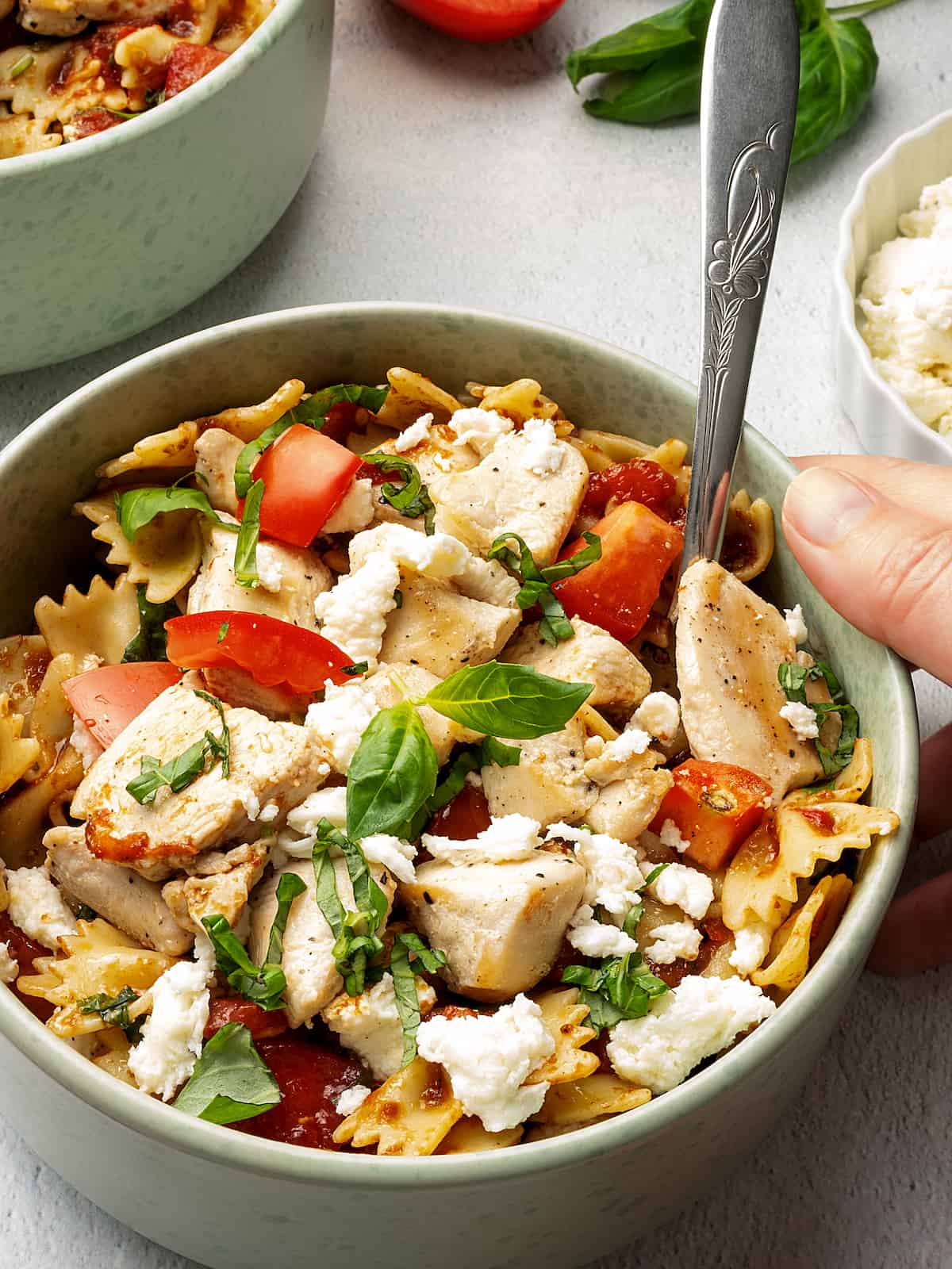 Chicken, diced tomato, chopped basil and bowtie noodles in a bowl with a spoon.