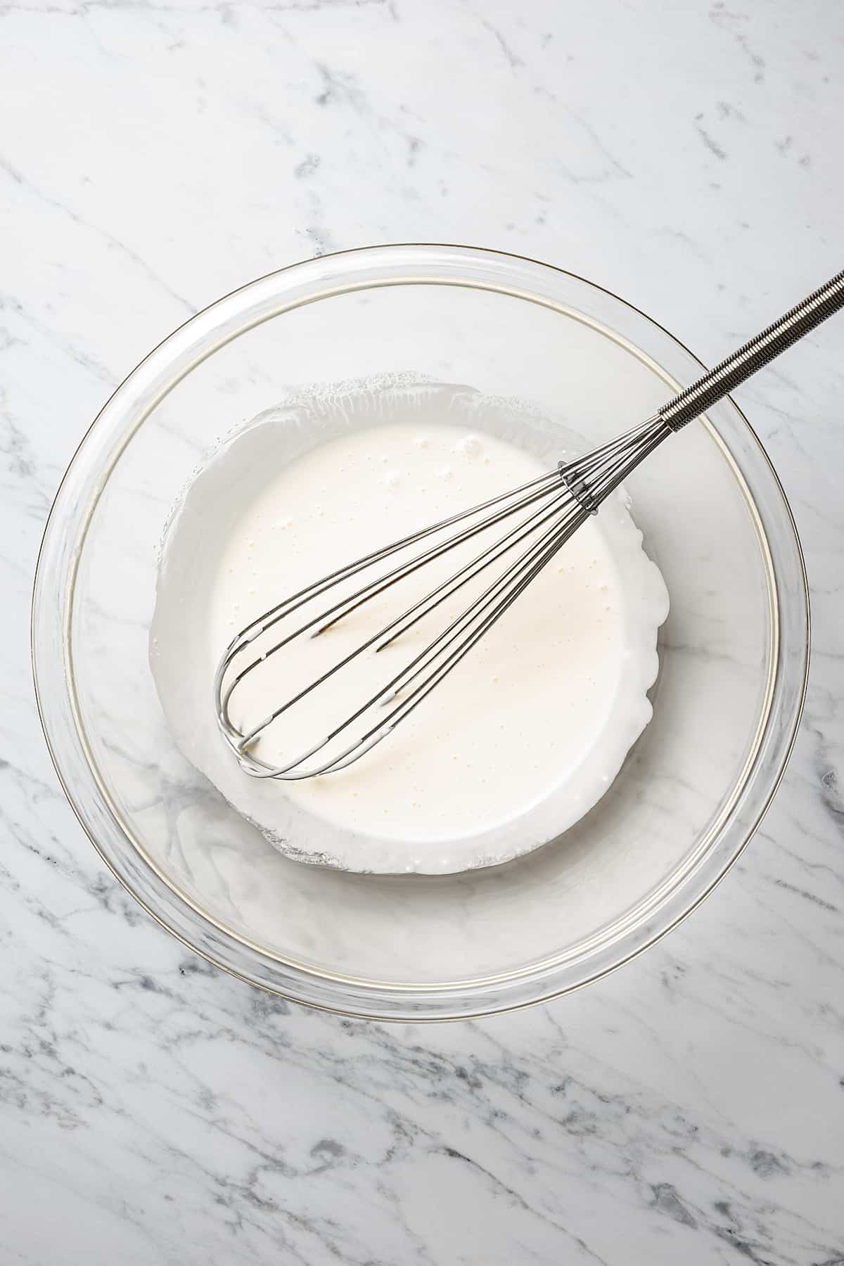 A creamy sauce in a mixing bowl, with a whisk.