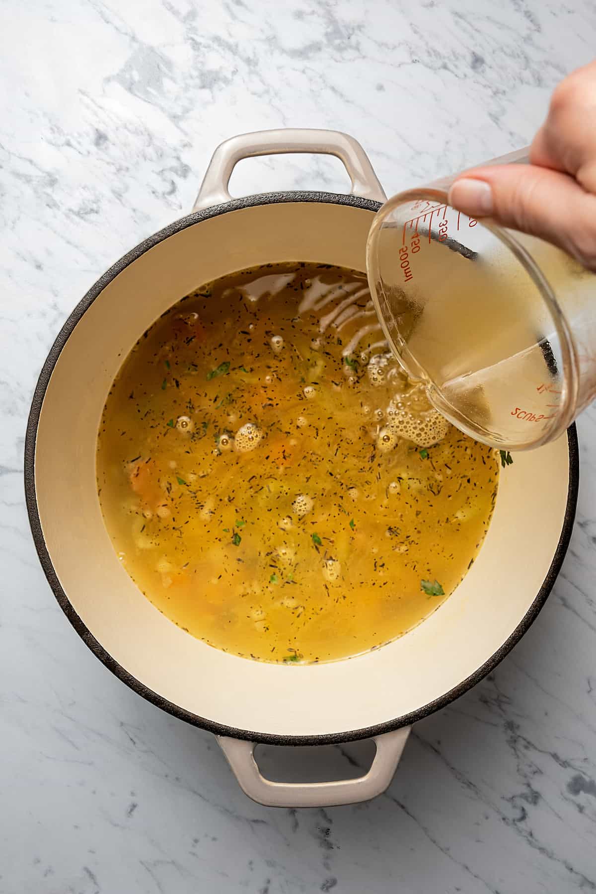 Pouring chicken broth into a pot.