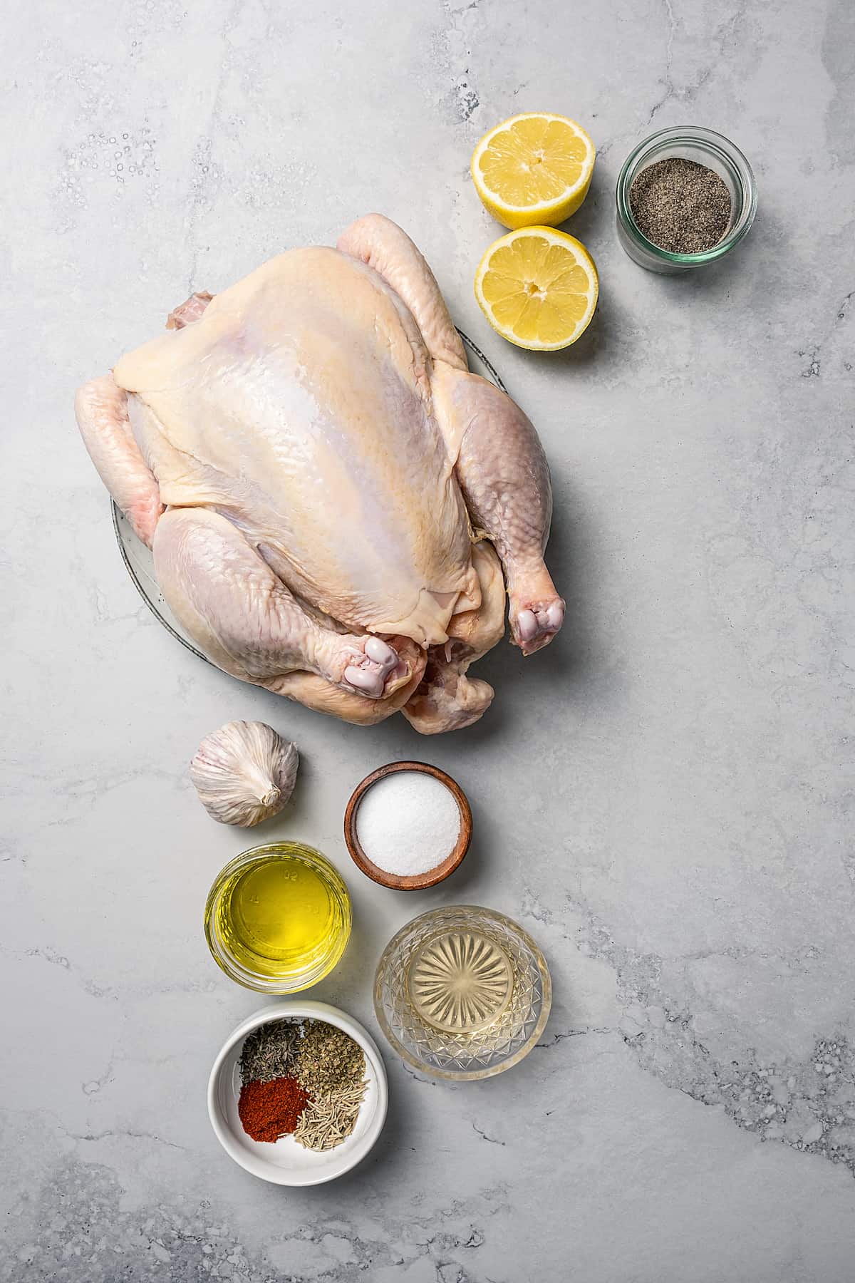 From top: Lemons, black pepper, a whole chicken, garlic, salt, olive oil, vinegar, spices.