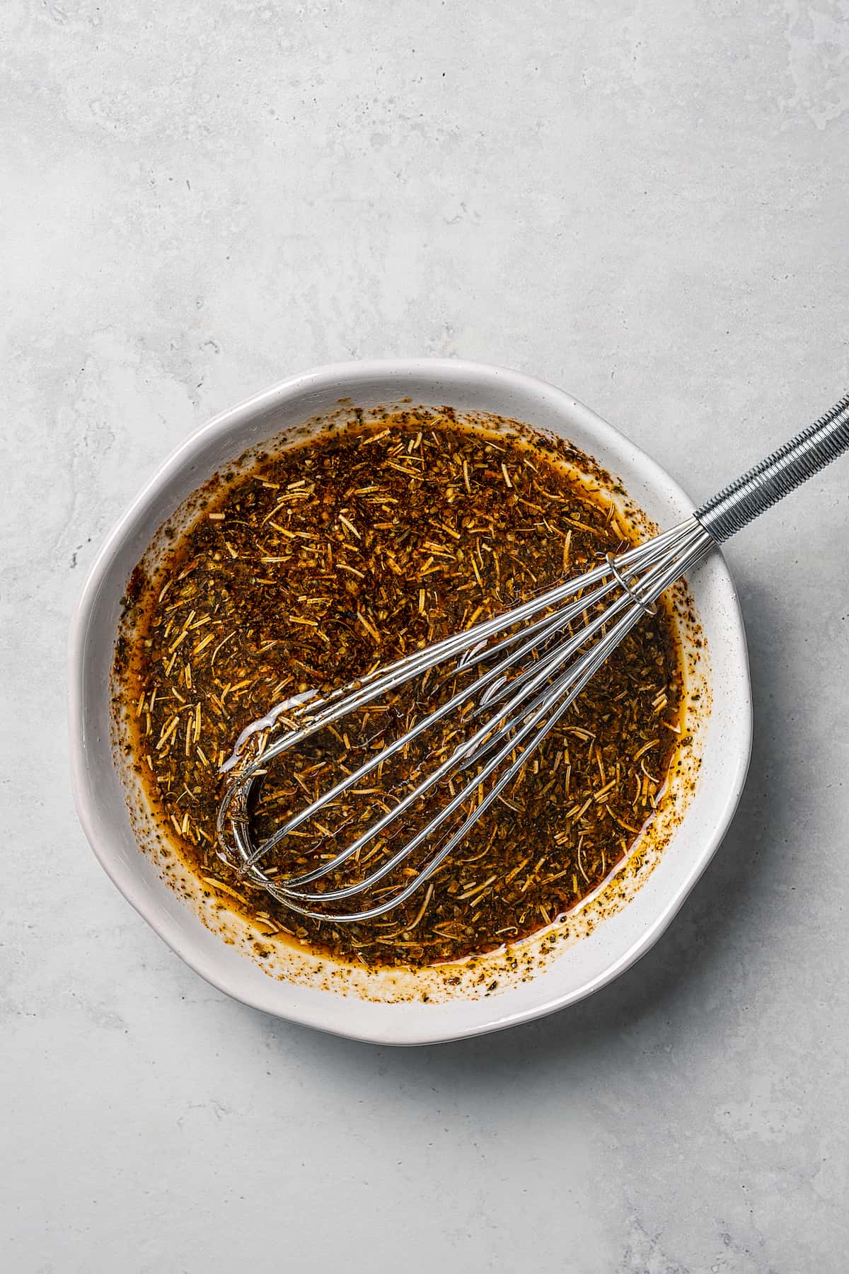 A spice and herb dressing in a small bowl, with a whisk.