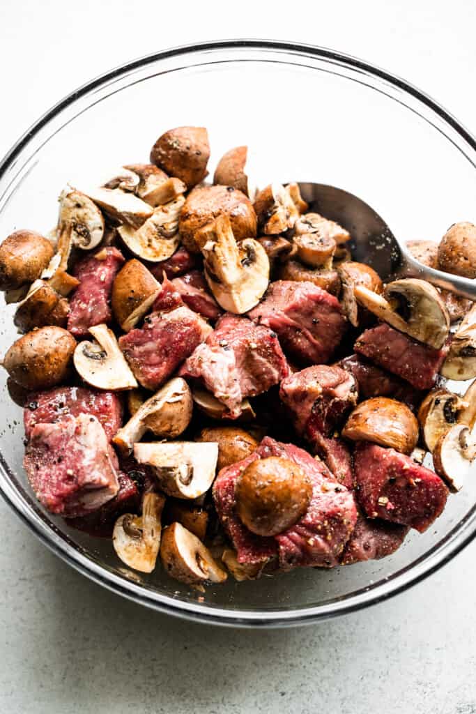 raw steak chunks and quartered bella mushrooms in a glass mixing bowl.