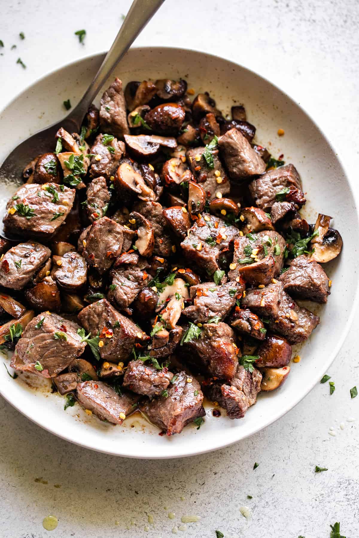 air fryer steak bites and mushrooms served in a round white serving platter, with a large spoon positioned at the top left of the platter.