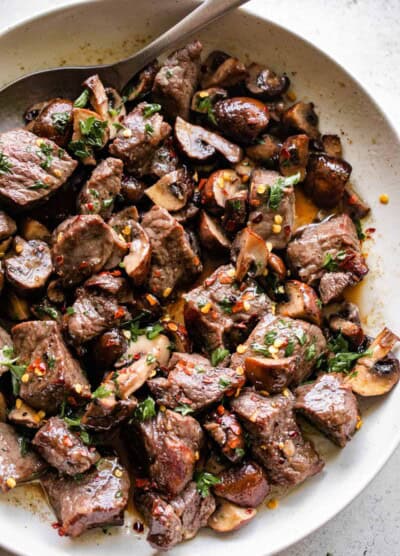 up close shot of air fryer steak bites and mushrooms served in a round white serving platter.