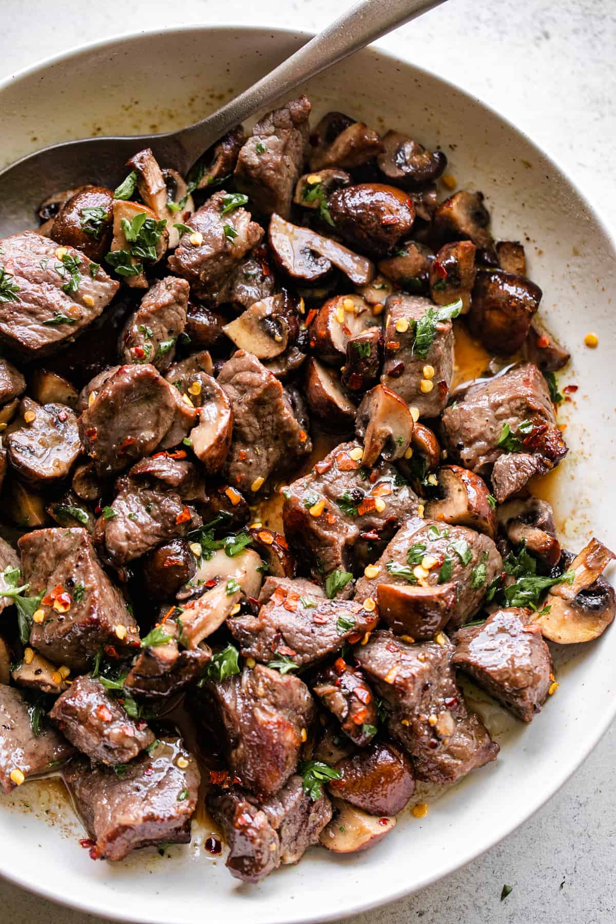 up close shot of air fryer steak bites and mushrooms served in a round white serving platter.