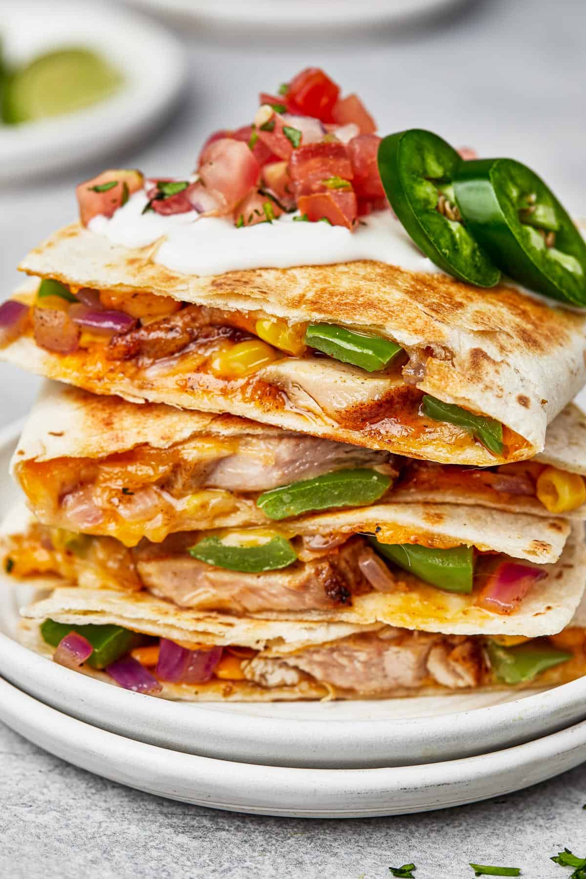 a stack of four chicken quesadillas topped with a garnish of tomatoes and peppers.