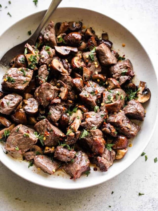 air fryer steak bites and mushrooms served in a round white serving platter, with a large spoon positioned at the top left of the platter.