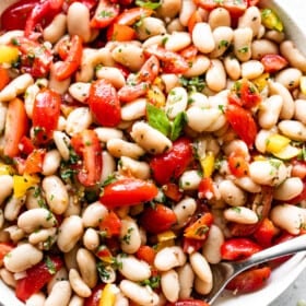 overhead shot of a salad bowl with cannellini beans, tomatoes, bell peppers, and a spoon set inside the right bottom side of the bowl.